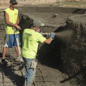 two men spraying gunite into a swimming pool during installation