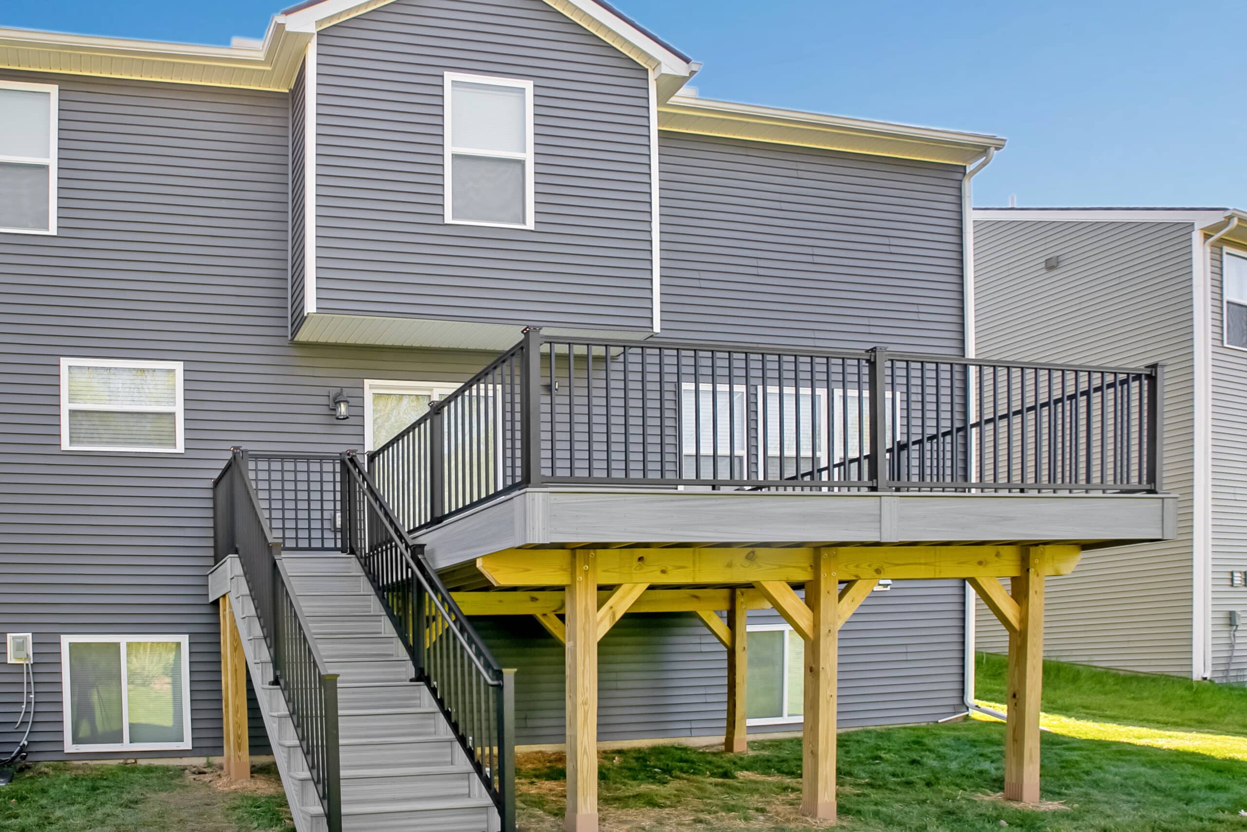 View of a home with a new deck with gray boards, black railings, and yellow support posts.