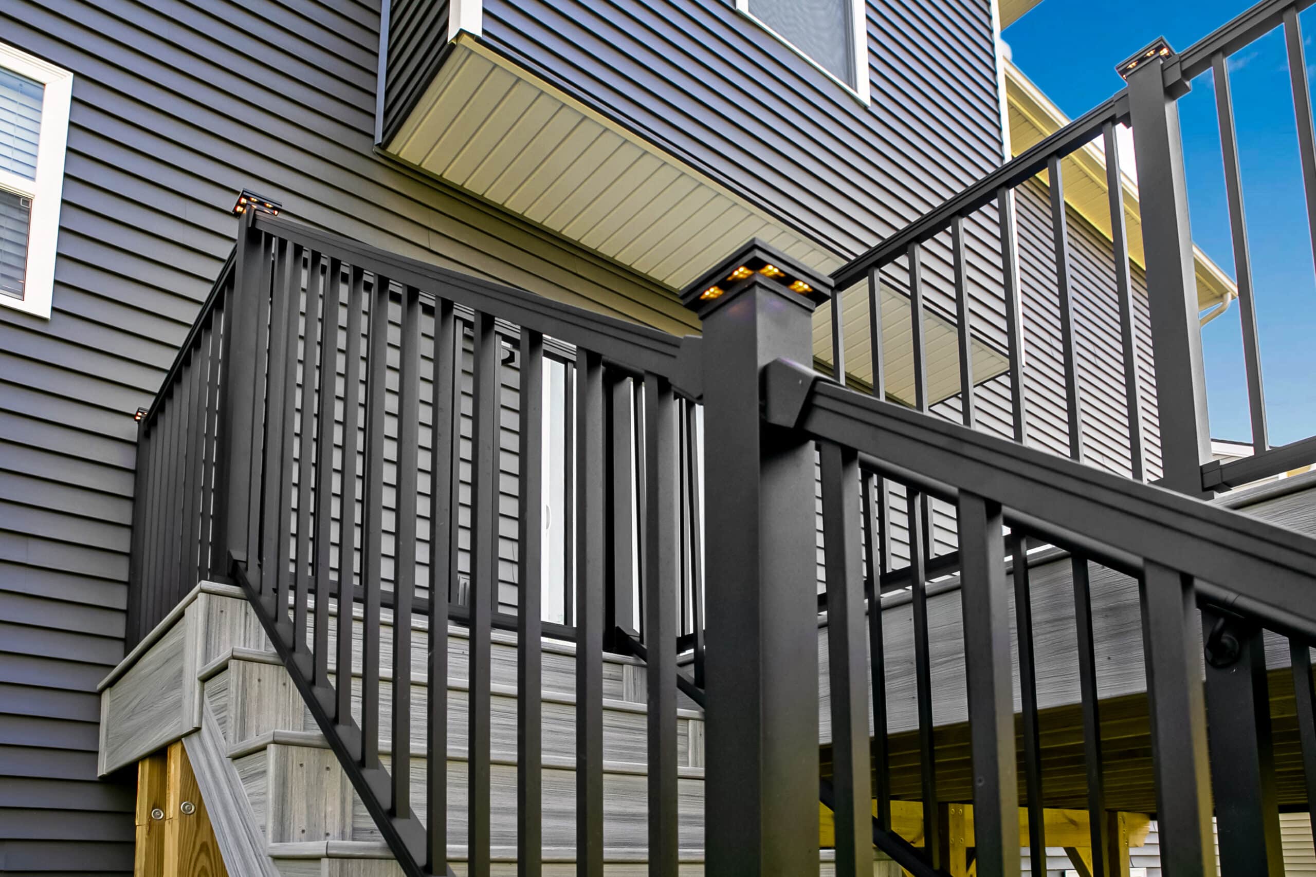 View of a home with a new deck with gray boards, black railings.
