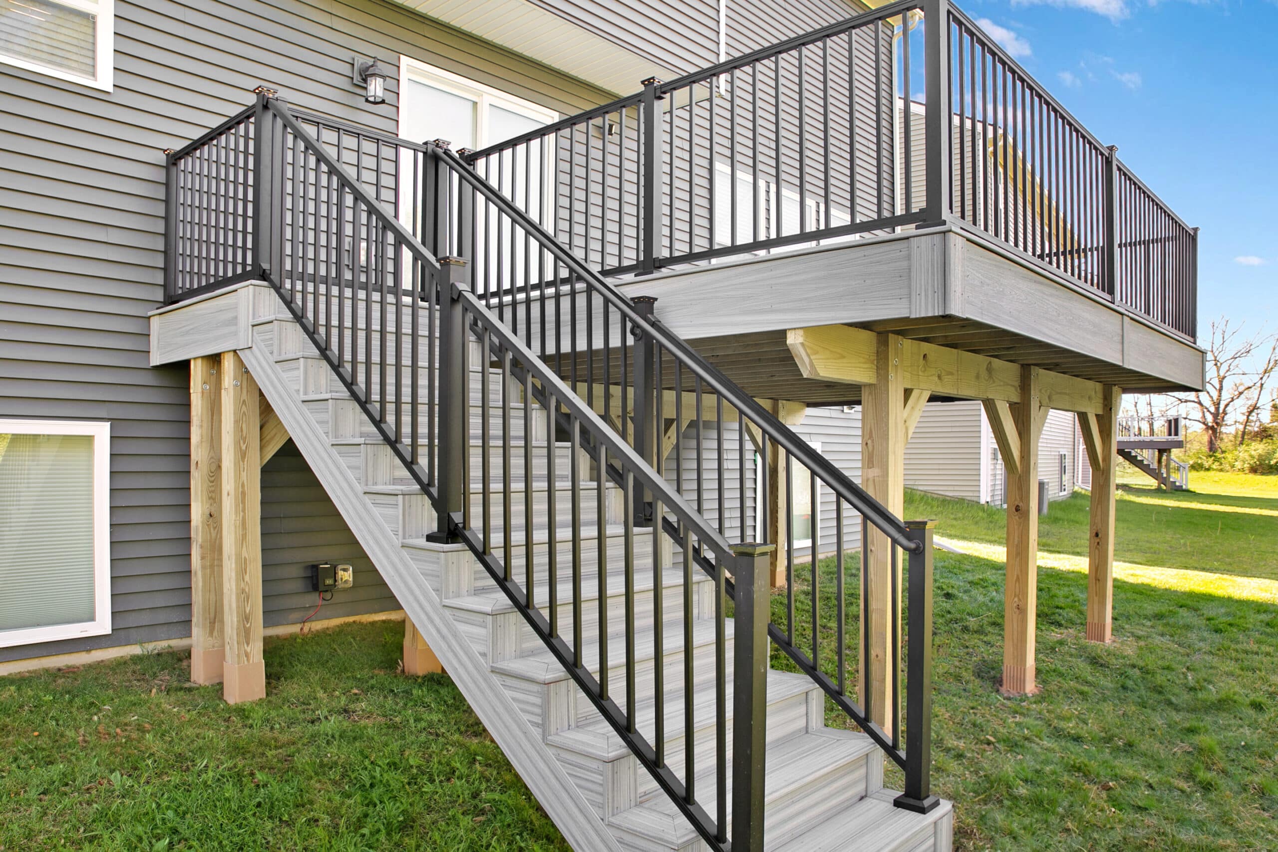View of a home with a new deck with gray boards, black railings, and yellow support posts.