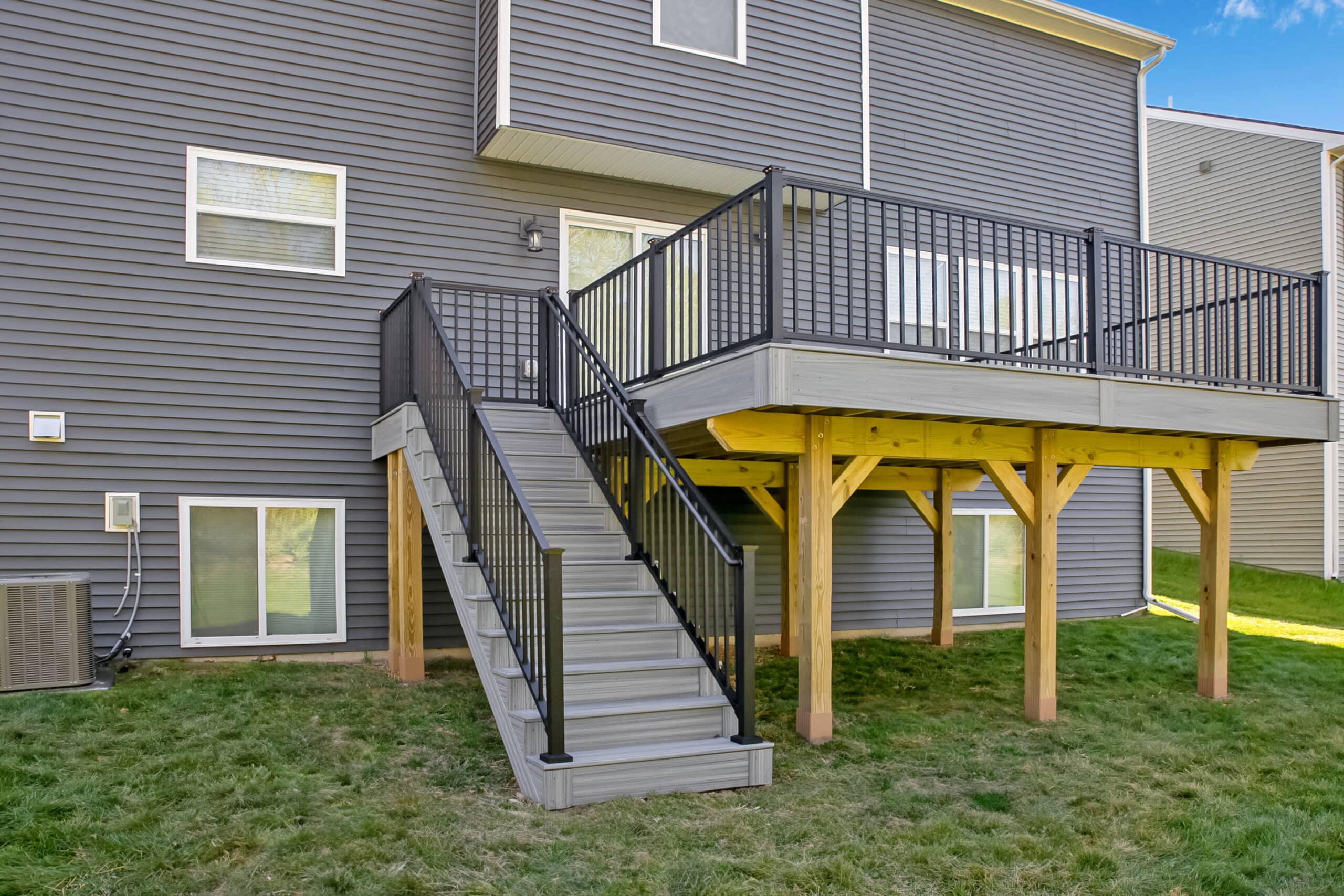View of a home with a new deck with gray boards, black railings, and yellow support posts.
