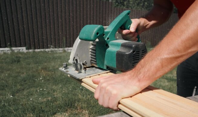 Close up of a man cutting deck boards with an electric saw.